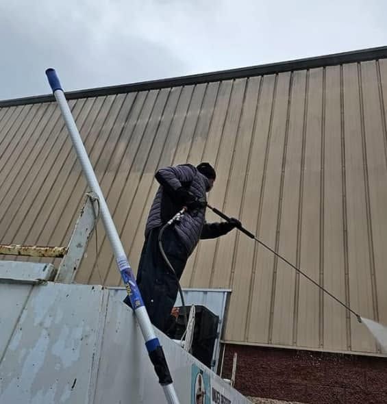 Worker on a ladder using a hose or cable against a beige building wall