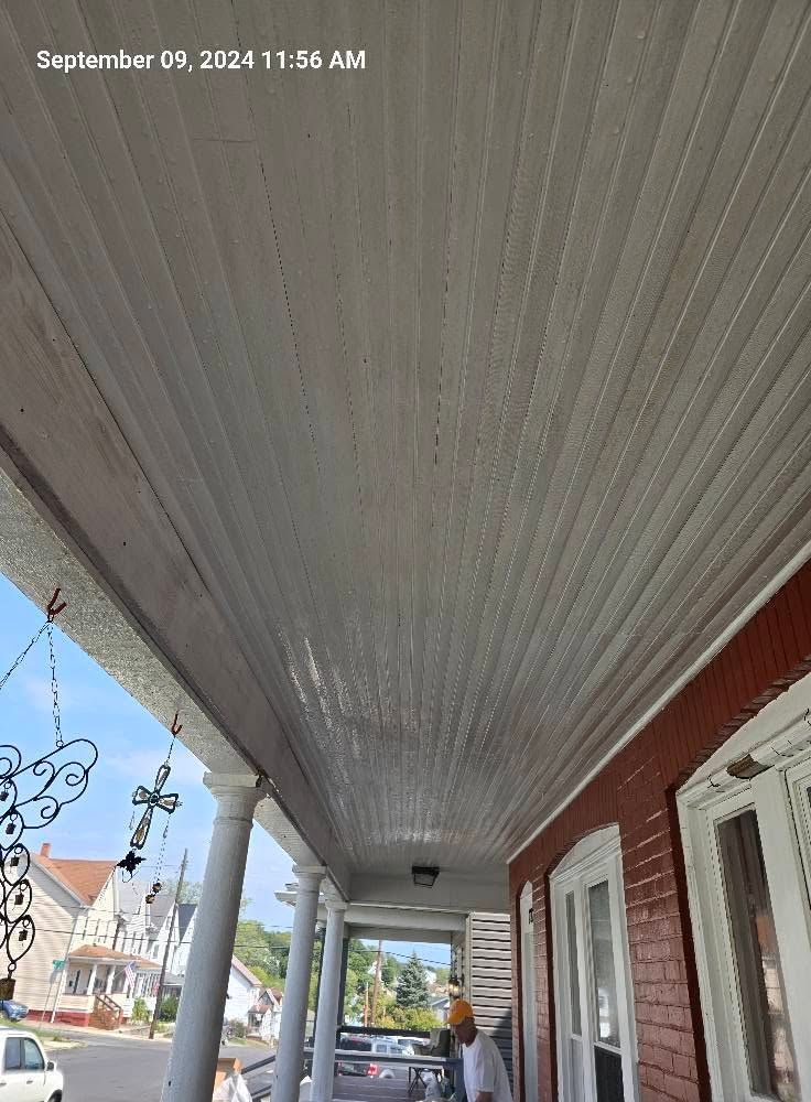 Covered porch with gray ceiling, red brick wall, white windows, and a view of houses and sky ahead