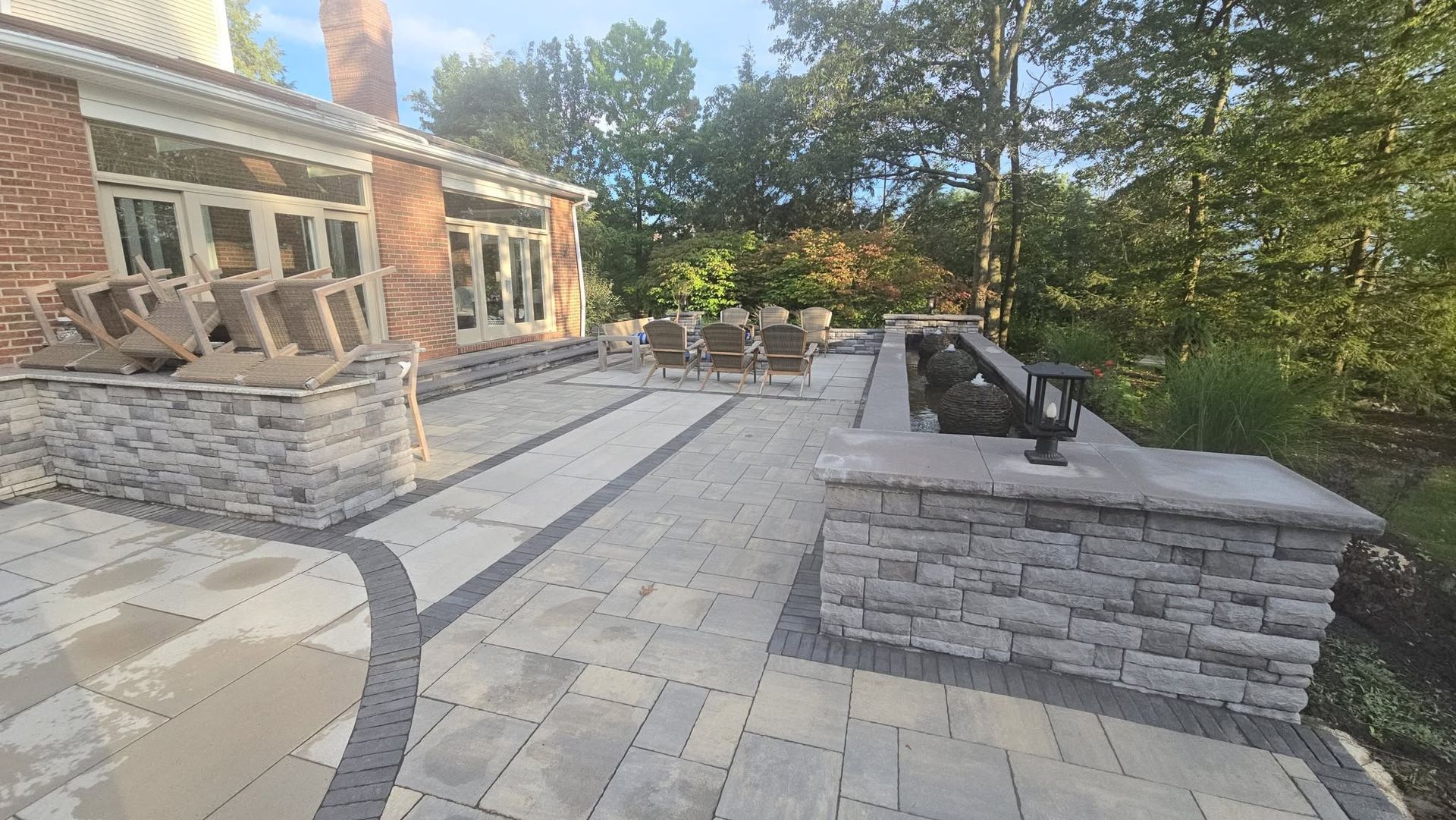 Patio with stone pavers, built-in seating, and fire pit beside a brick house and trees