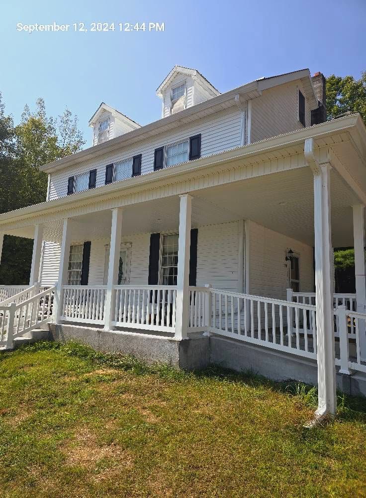 White historic house with a wraparound porch and white railings on a sunny day