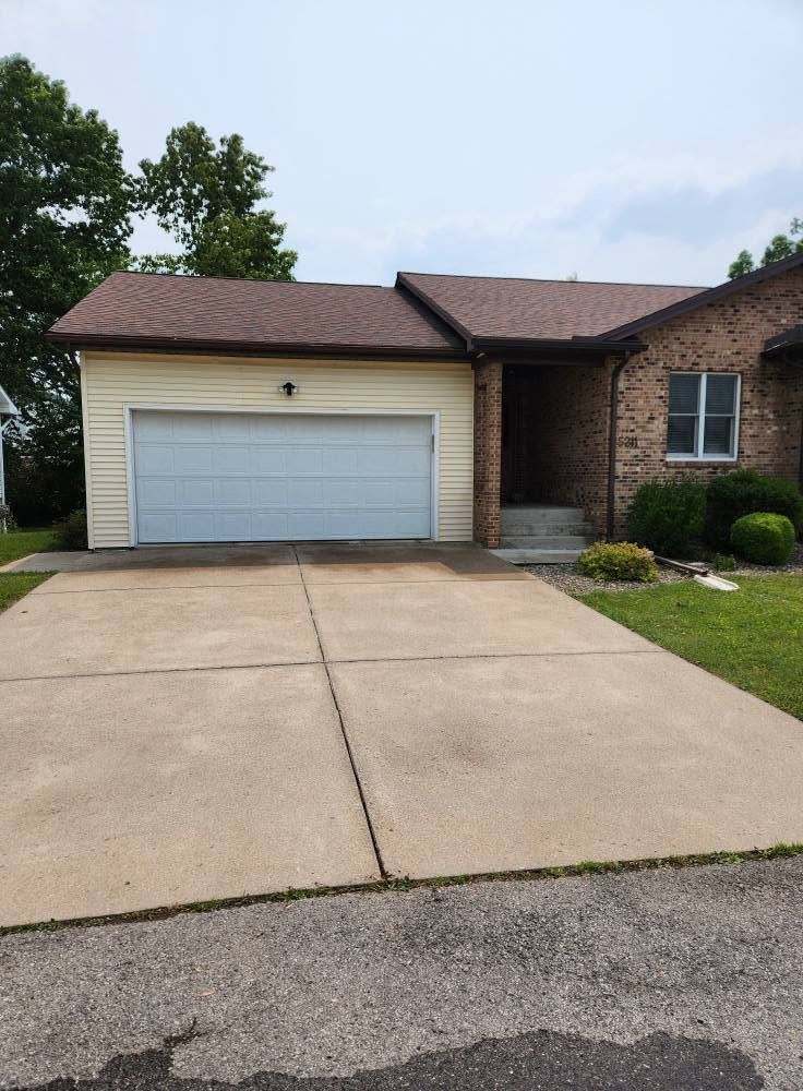 Suburban brick house with two-car garage, concrete driveway, and small front lawn
