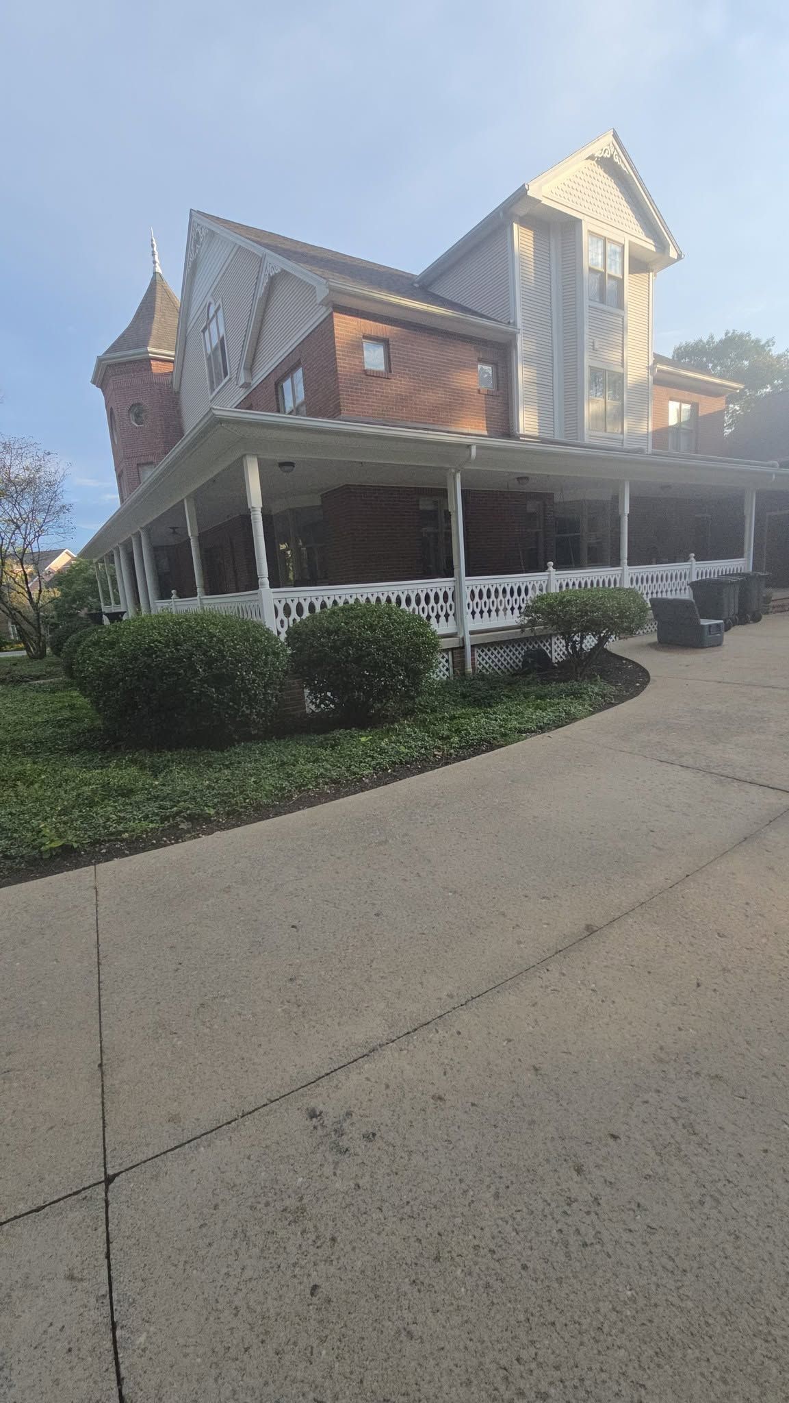 Historic house with wraparound porch, white columns, and brick exterior beside a sloped driveway