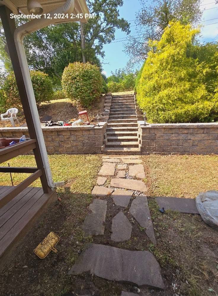 Stone path and steps leading to a raised garden patio with brick walls and green shrubs.