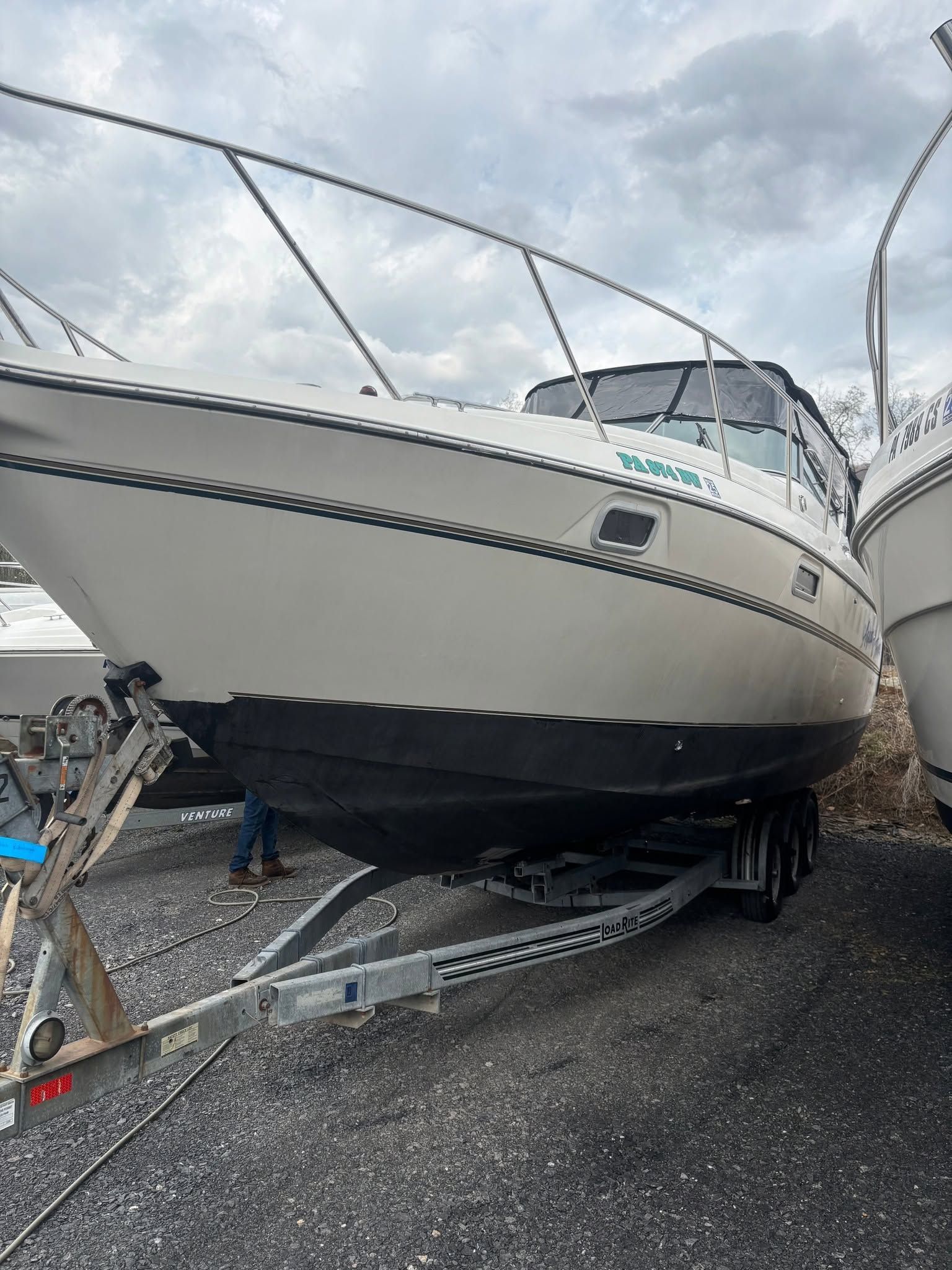 White sailboat on a trailer in a boatyard, with a black hull and cloudy sky overhead