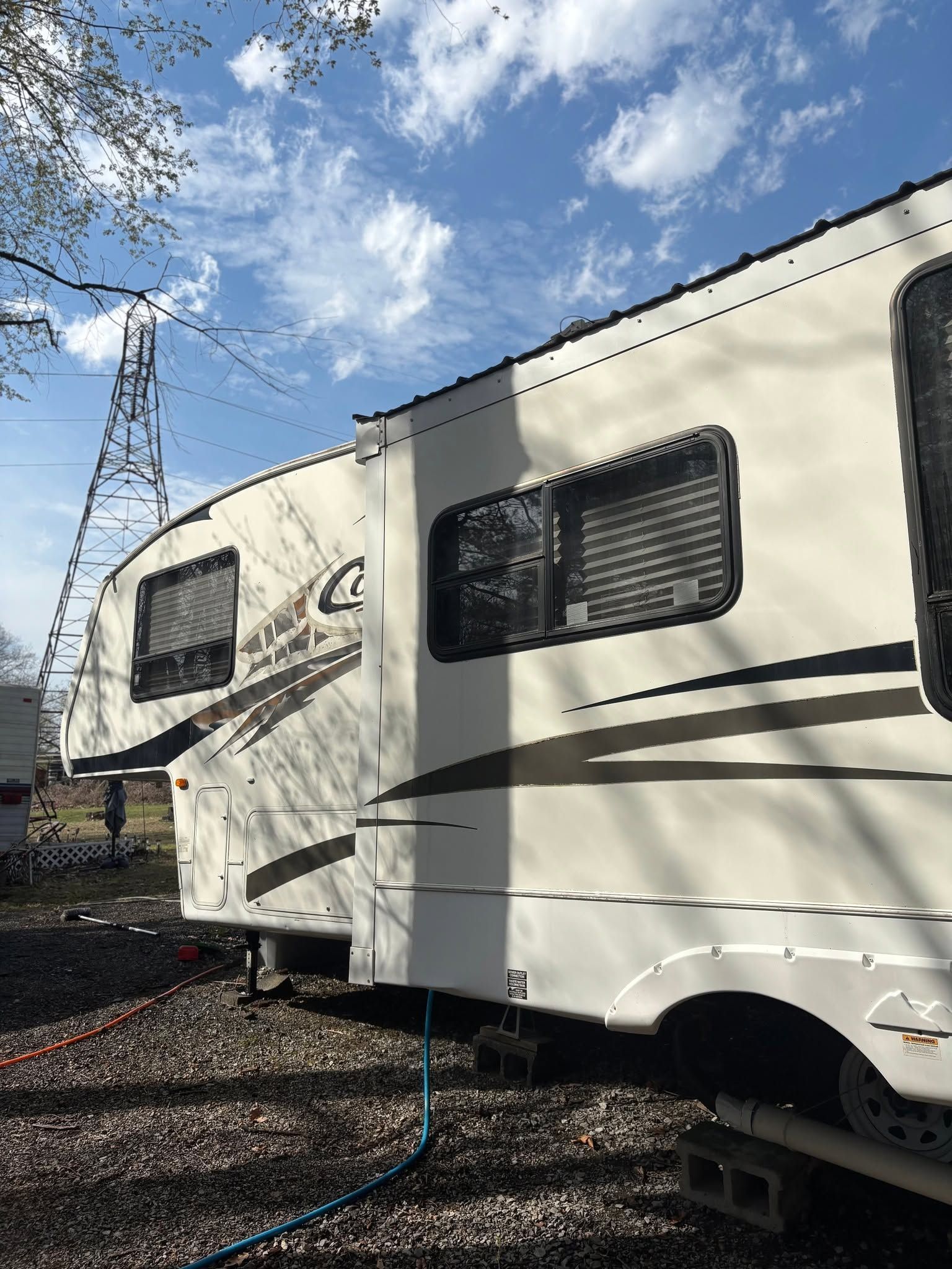 White RV trailer parked on gravel under a blue sky, with windows and a power cable visible