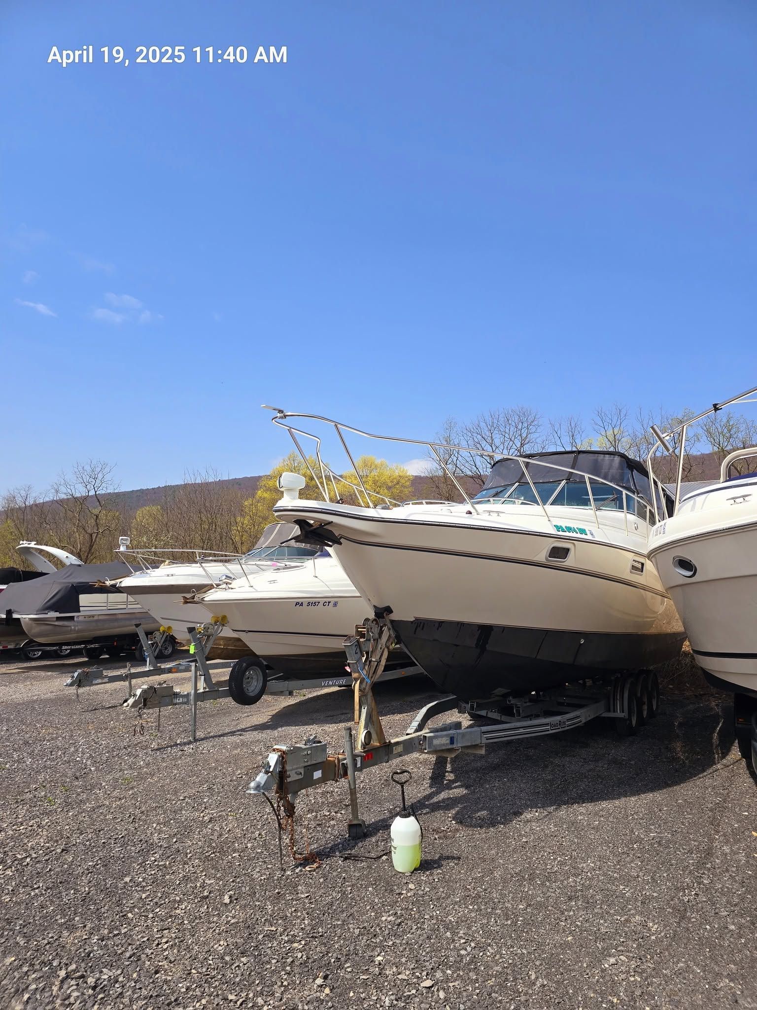 Boats stored on gravel under a bright blue sky, with snow patches around them.