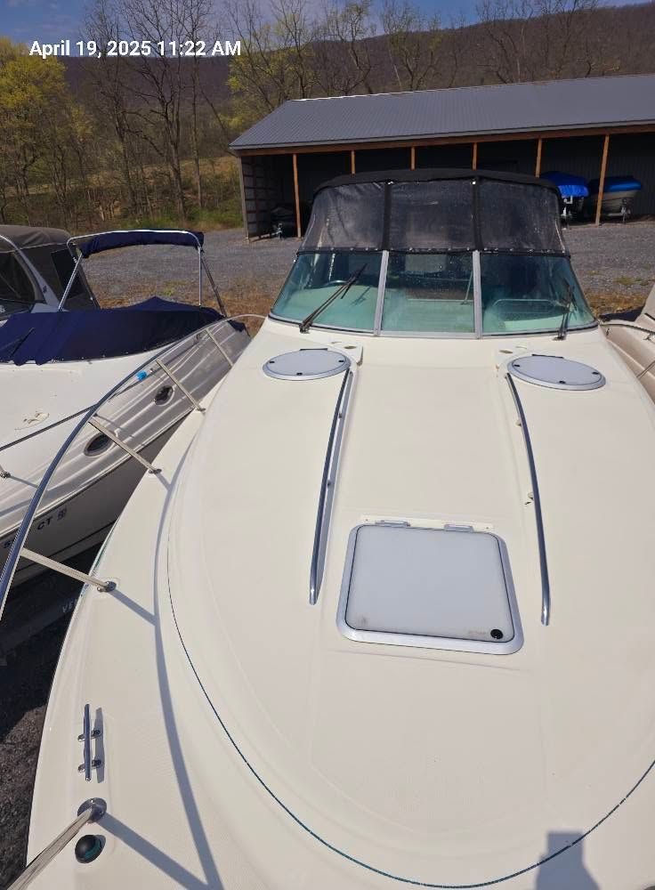 White boat deck with windshield and hatches docked beside another boat near a boathouse.