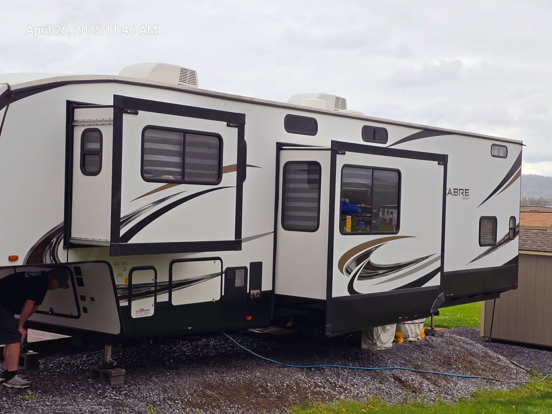 White and black travel trailer with slide-out parked on gravel under overcast sky