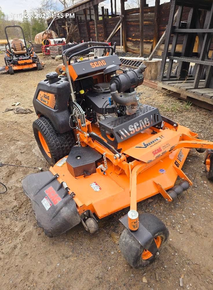 Orange zero-turn lawn mower with front attachment, parked in a workshop or yard area
