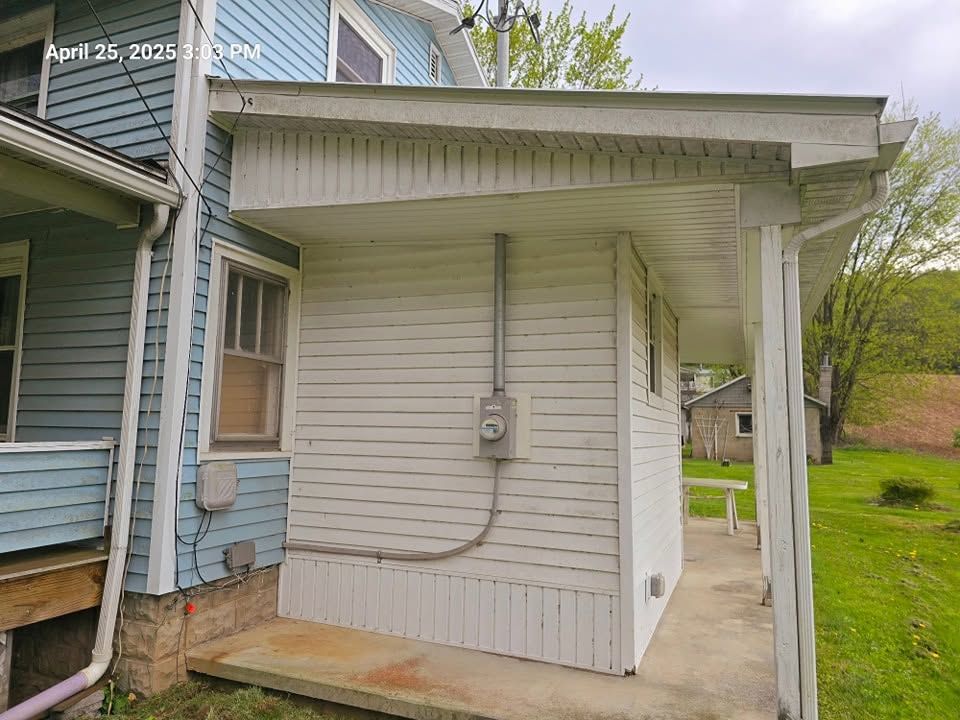 White-sided house exterior with a small covered porch, utility meter, and side walkway in a grassy yard