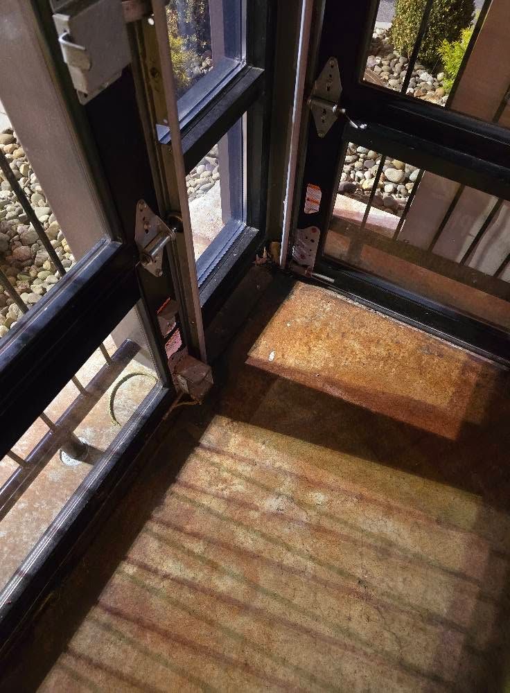 Sunlit enclosed porch with black window frames and shadows cast across a wooden floor.
