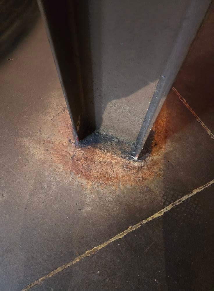 Rusty metal base of a post on a concrete floor with orange corrosion stains