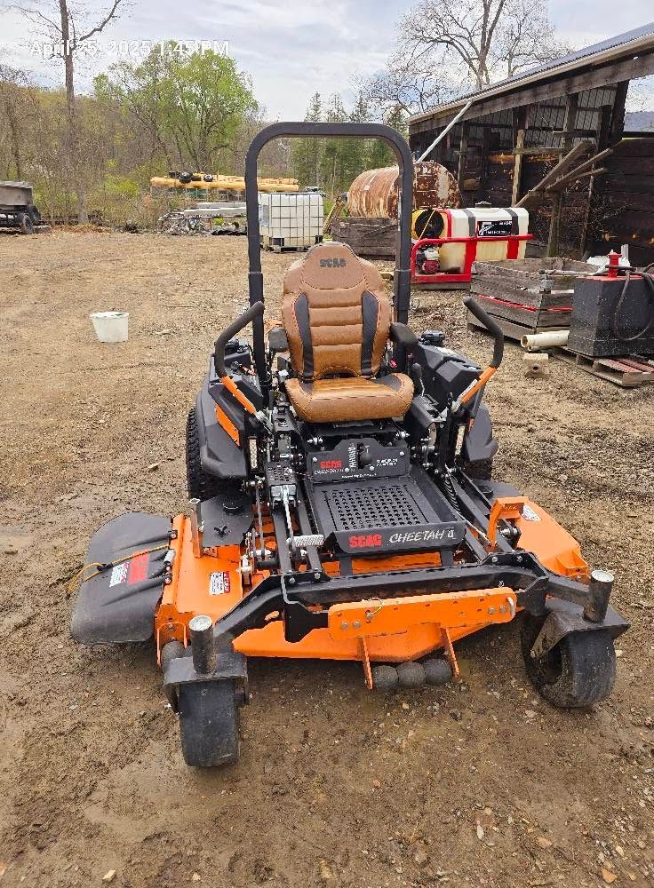 Orange zero-turn mower in a dirt yard beside a shed, with a beige seat and black roll bar.
