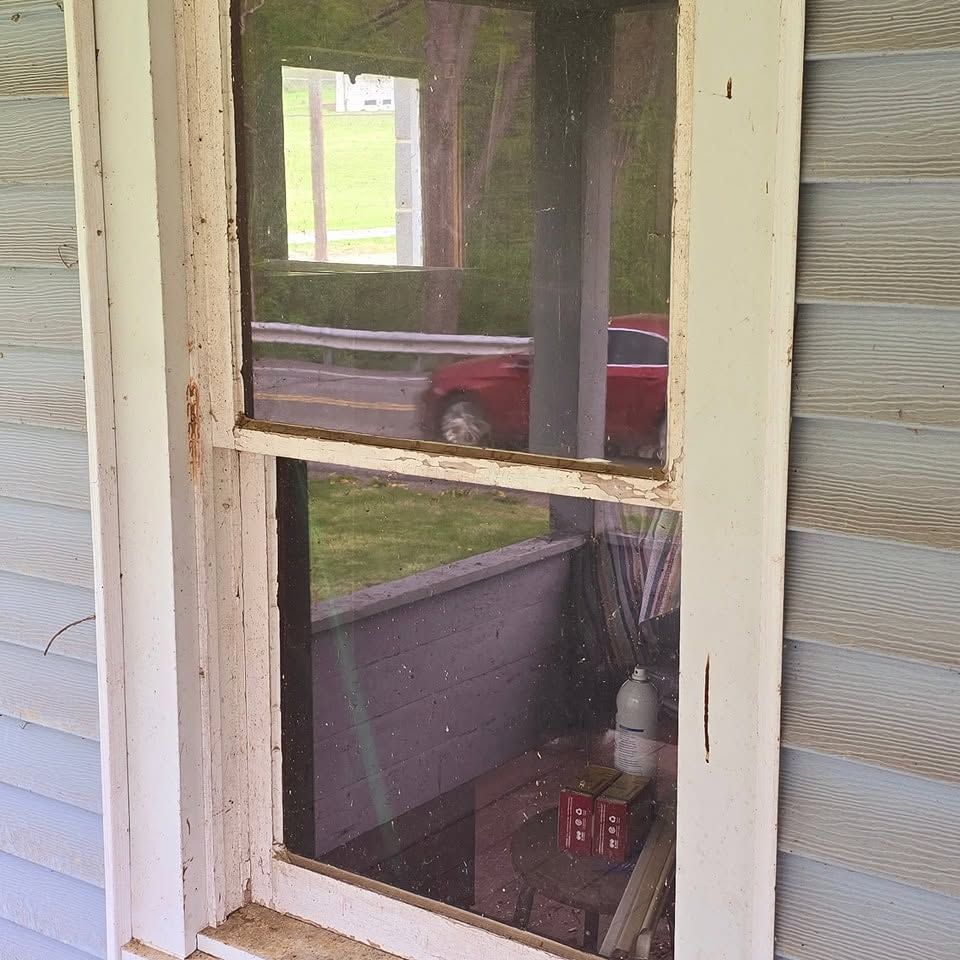 Weathered white window with screen, overlooking a porch and parked red car outside.