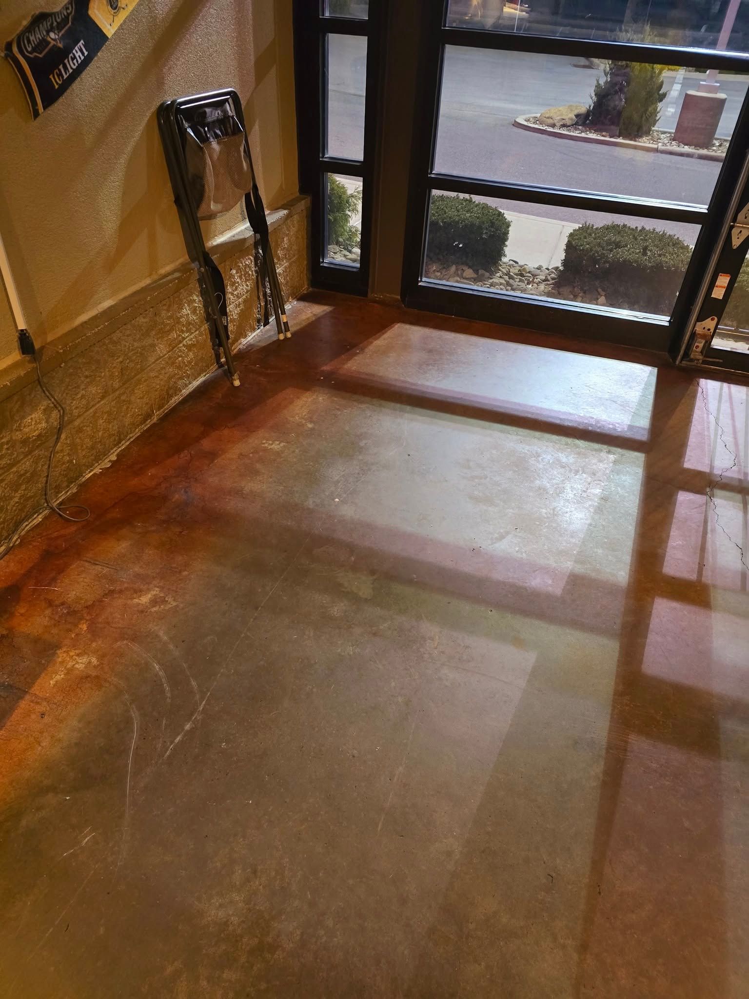 Wet lobby floor near glass doors with a caution sign and reflections from outside light