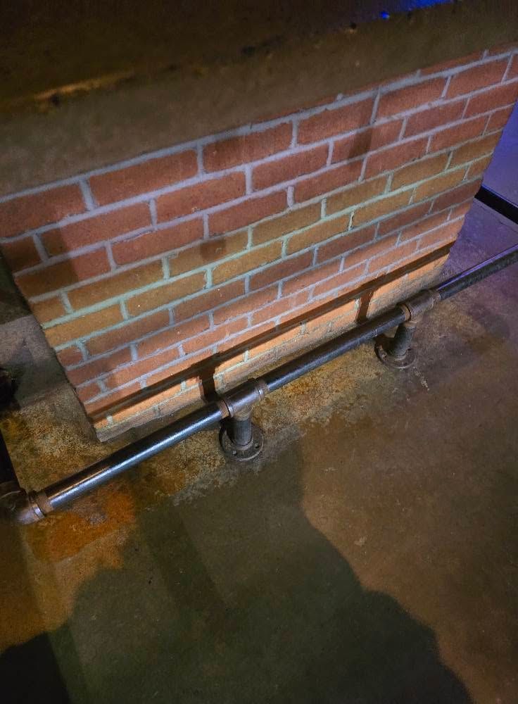 Brick wall with a metal handrail and supports over a wet concrete floor.
