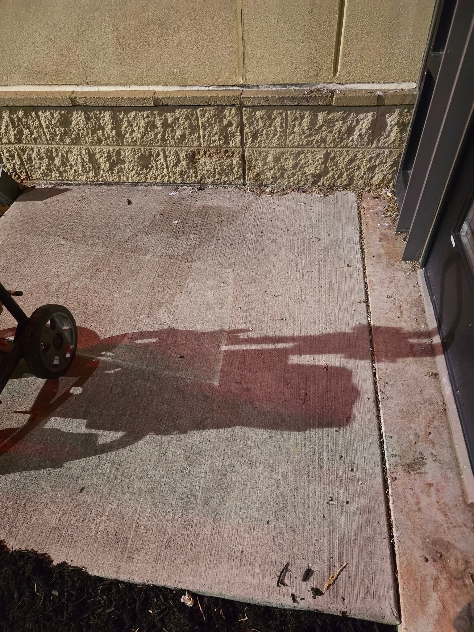 Red liquid spilled on a concrete patio beside a wall and door threshold.