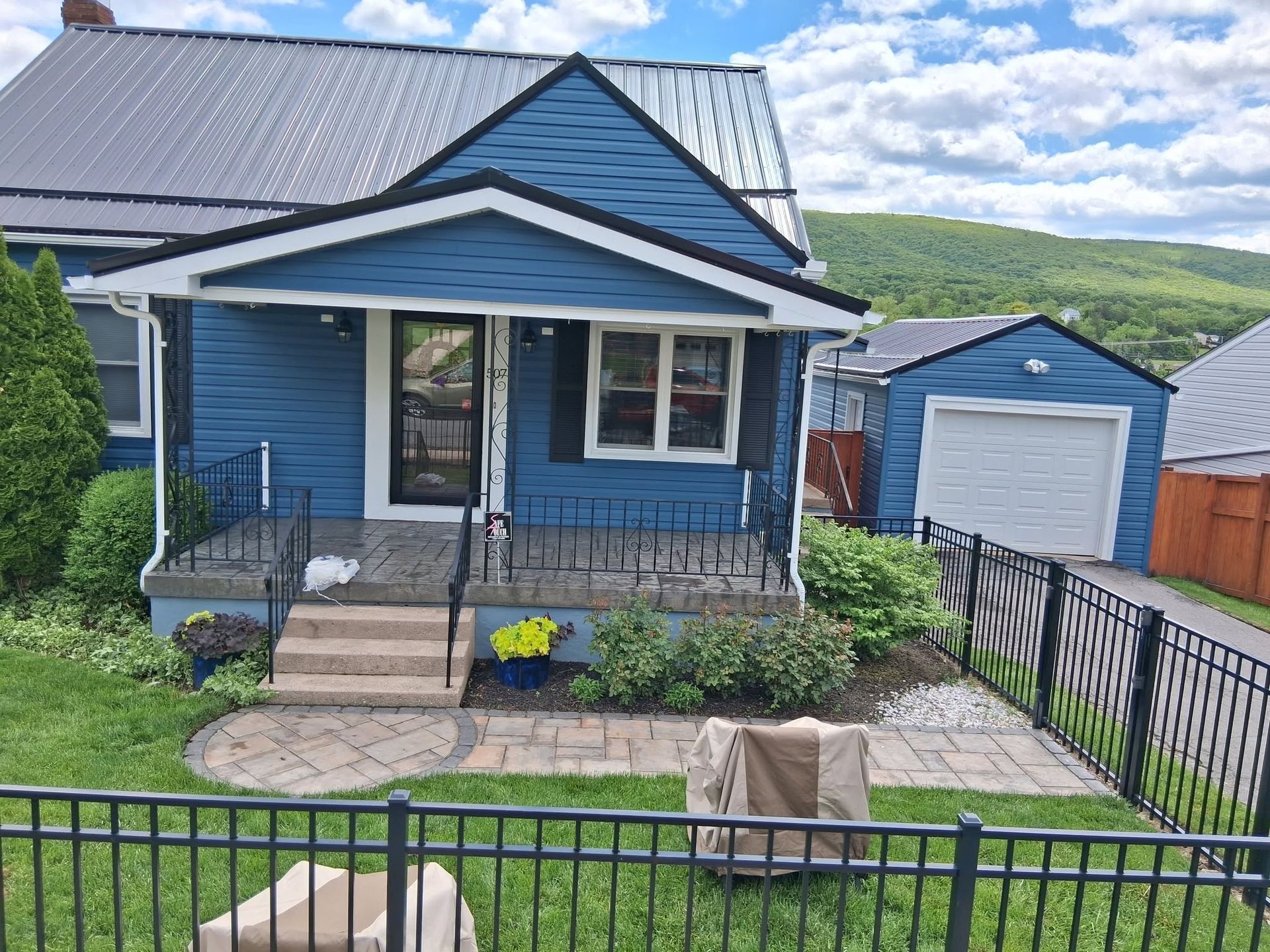 Blue house with a front porch, black railing, small garden, and a garage in the background