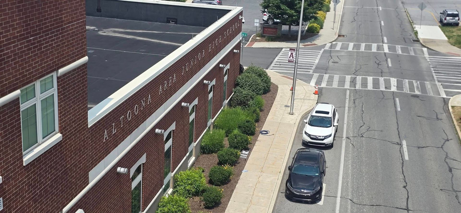 Aerial view of a brick building beside a street with parked cars and a crosswalk.