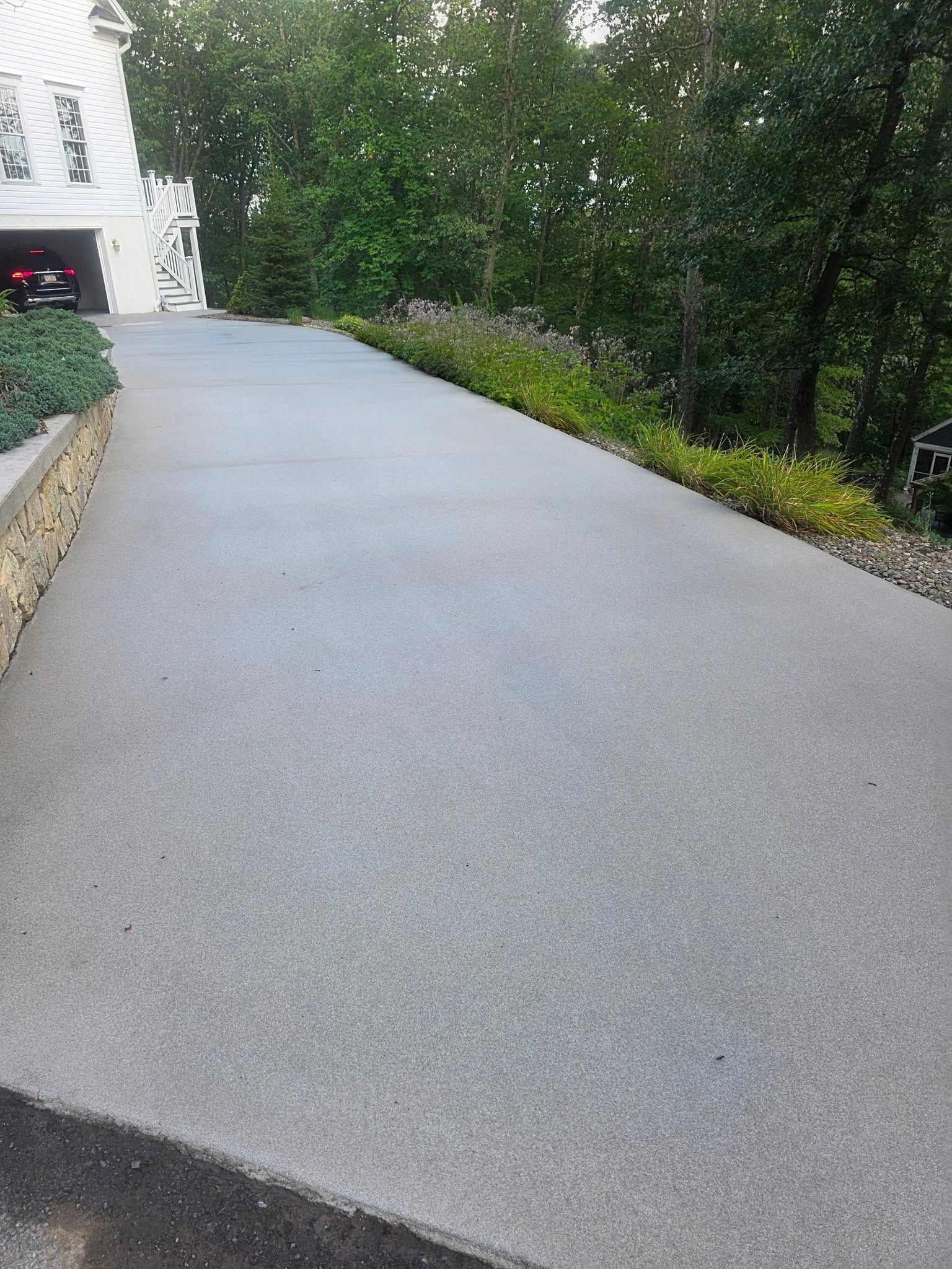 Freshly paved driveway beside a house, bordered by shrubs and trees