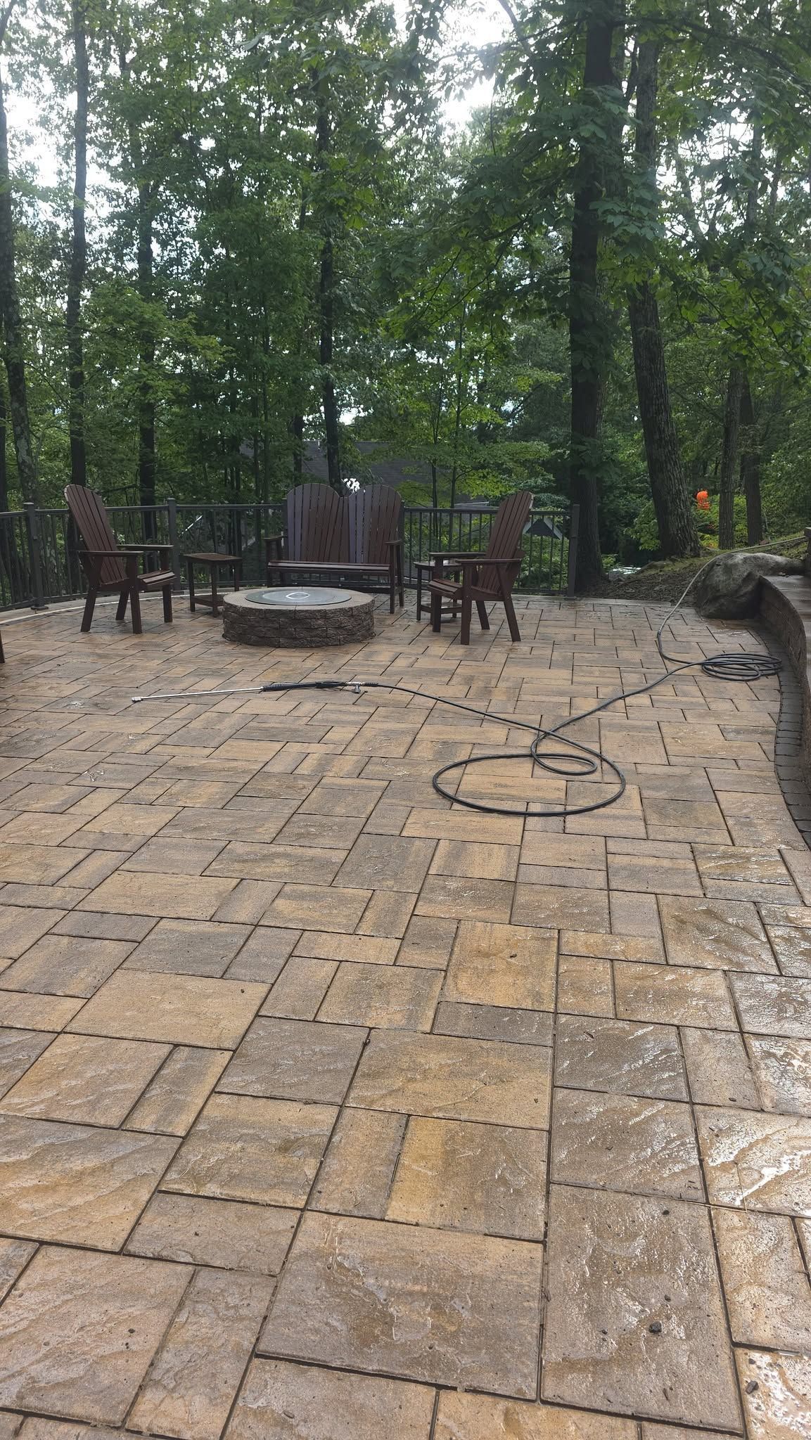 Brick patio with fire pit and wooden chairs in a wooded outdoor setting
