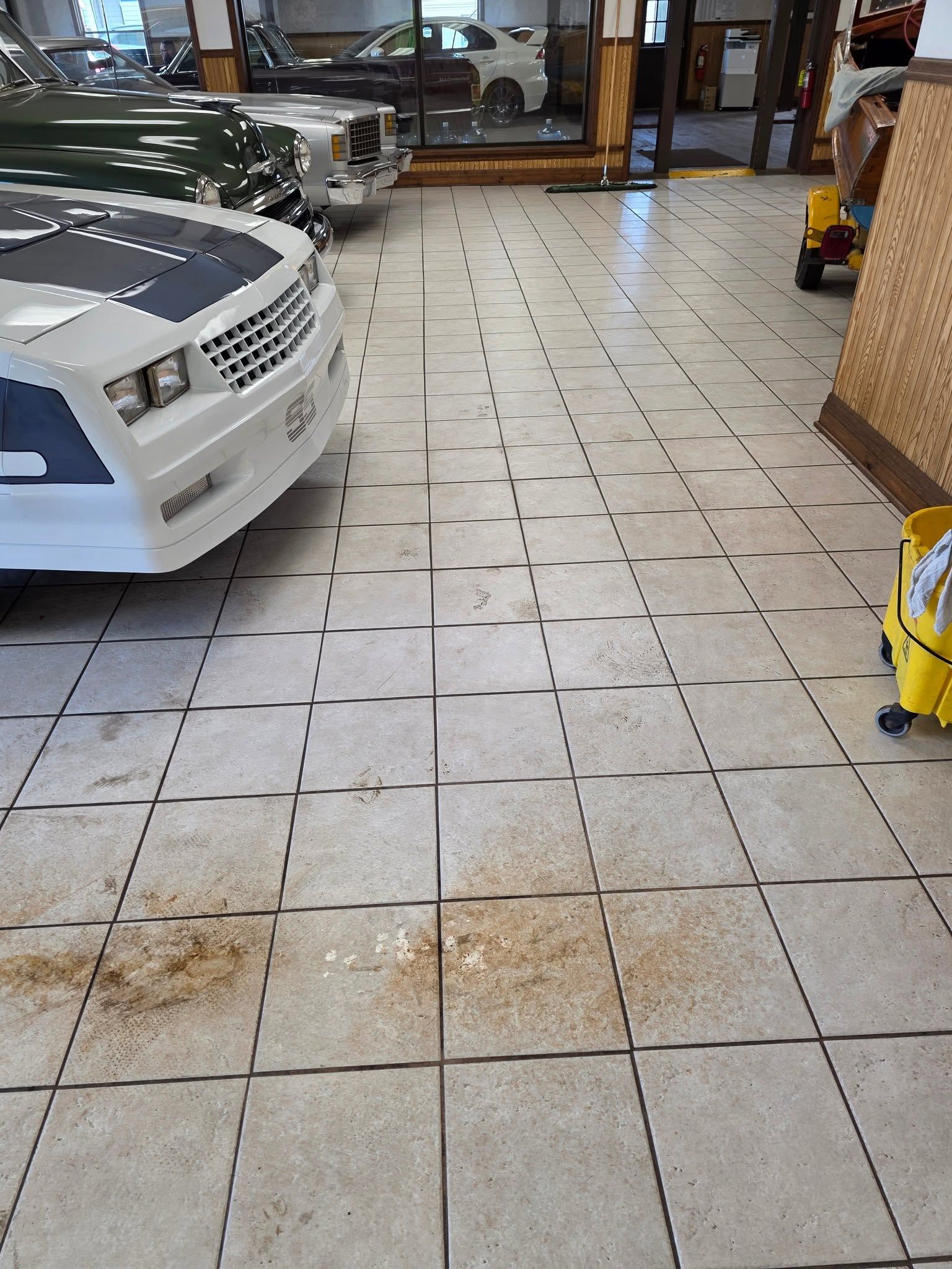 Car showroom with white car on the left and tiled floor leading to glass entrance.