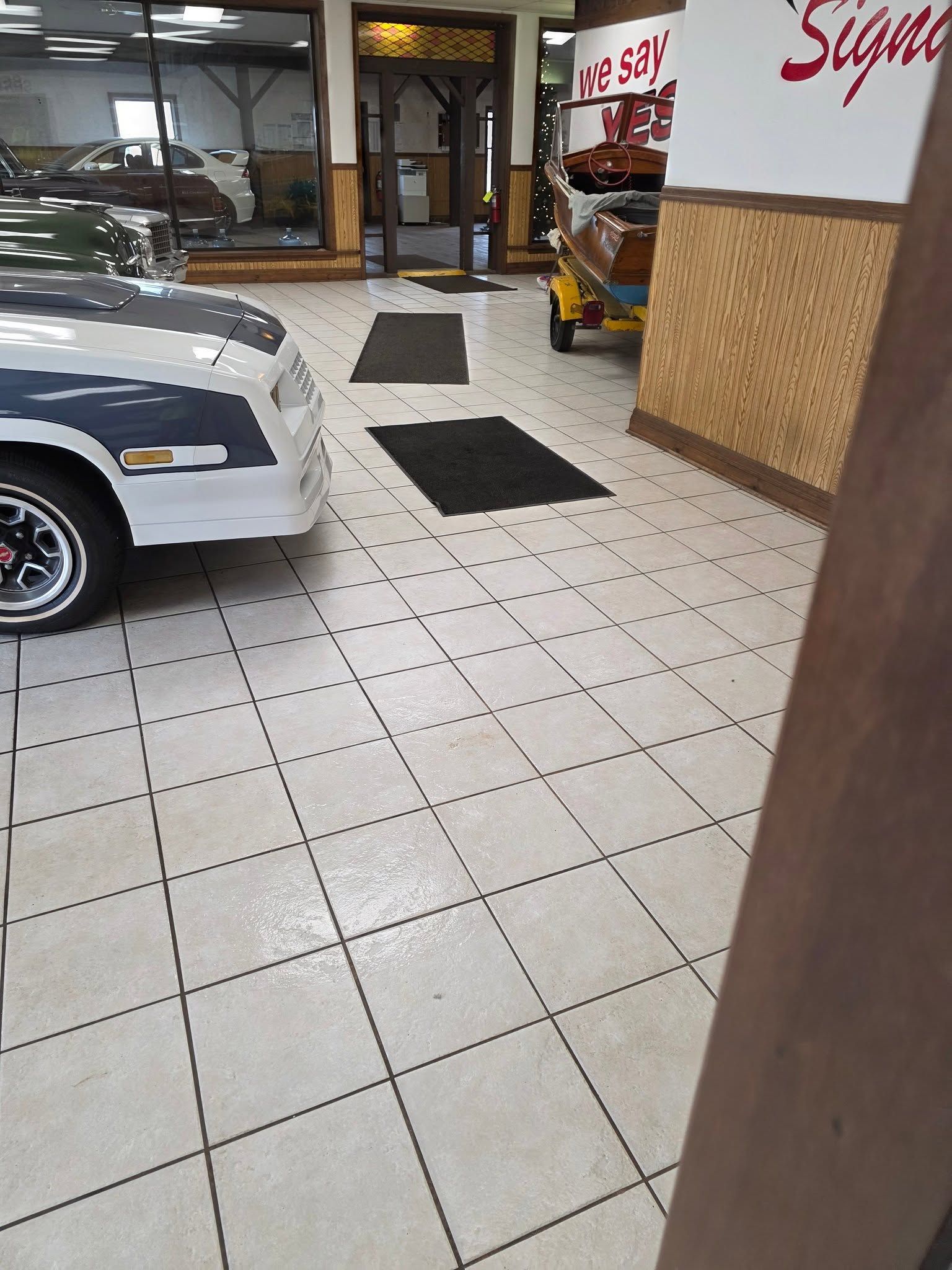 Car showroom interior with a white sports car, tiled floor, and storefront windows.