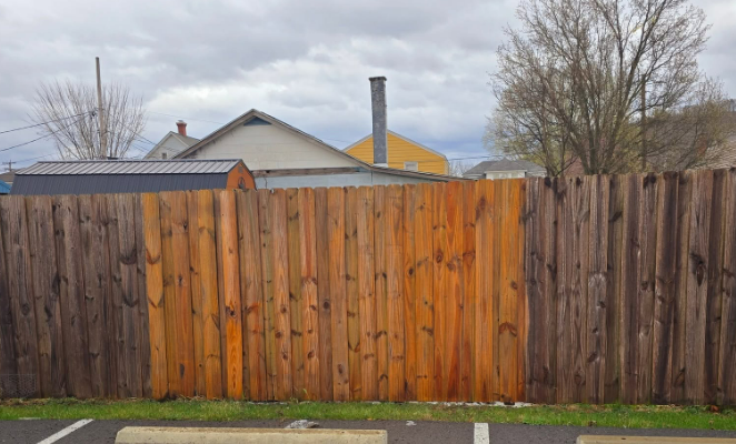 Wooden backyard fence with houses and leafless trees behind it under a cloudy sky