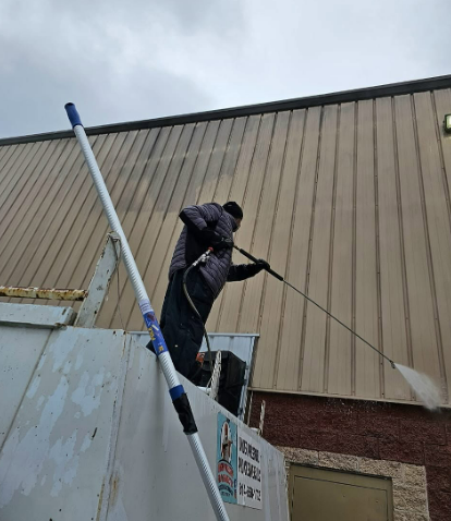 Worker on a ladder painting the side of a tall beige building.