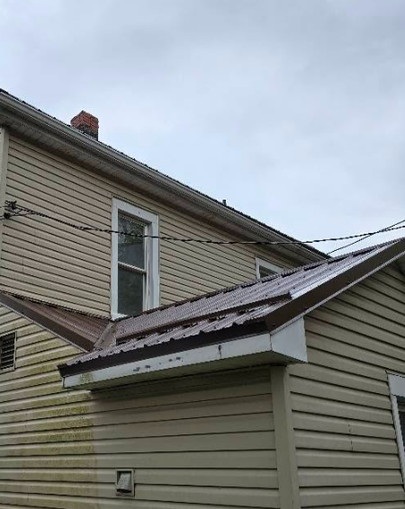 Side view of a beige house with white trim and a small sloped roof under a cloudy sky.