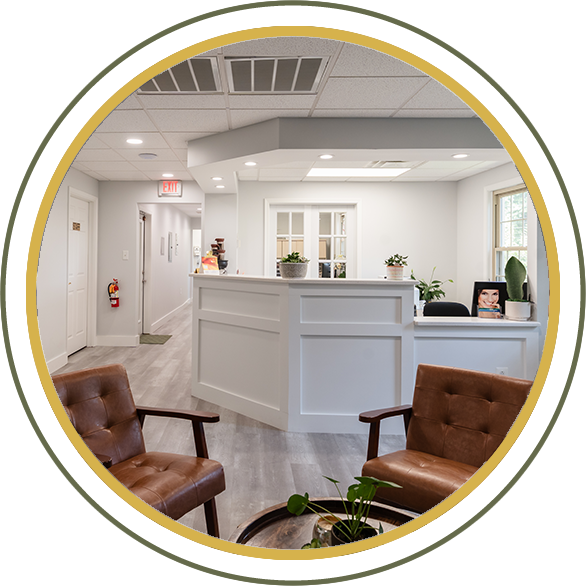 Reception area with white desk, two brown chairs, and plants.