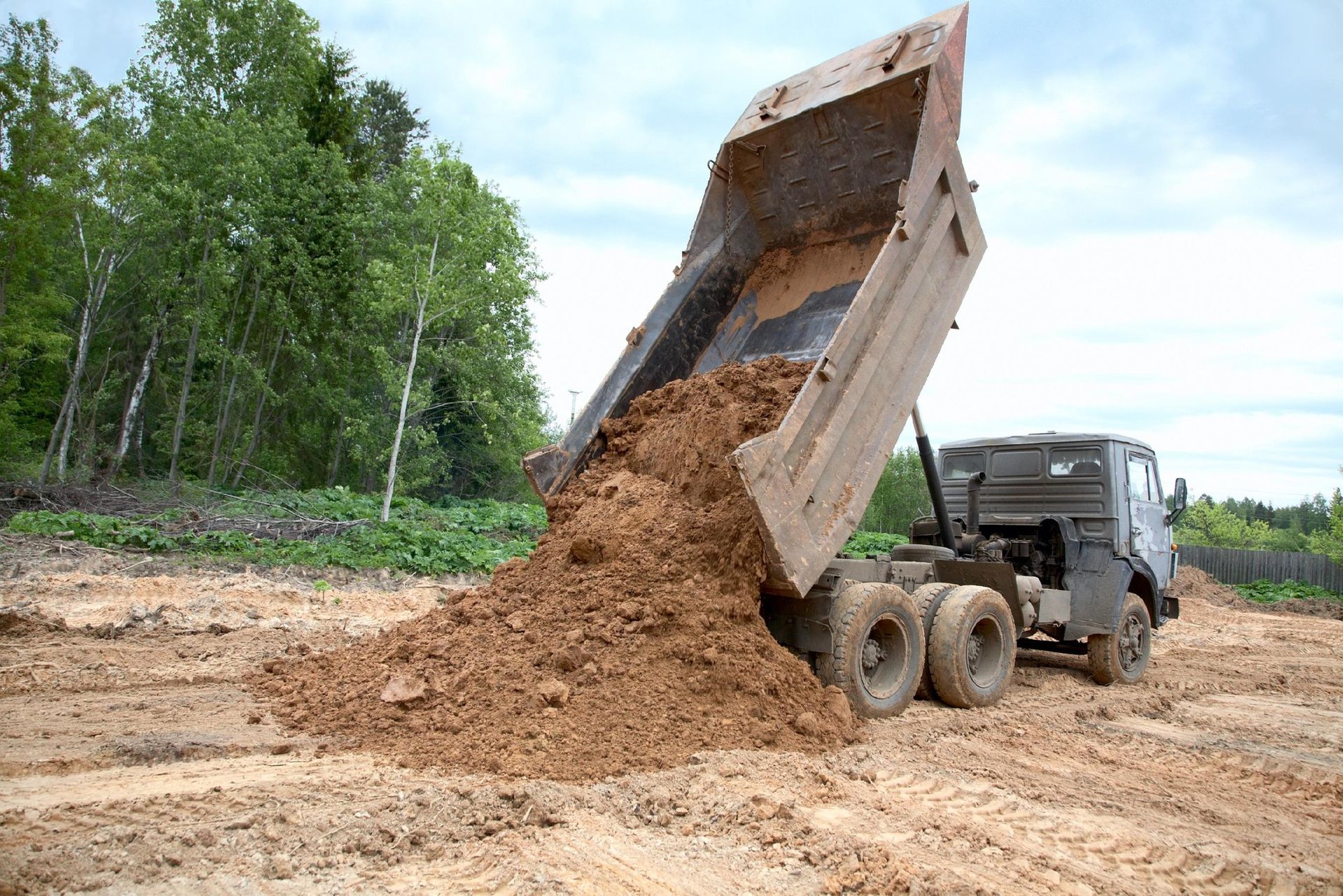 Dump truck unloading dirt at a construction site with trees in the background