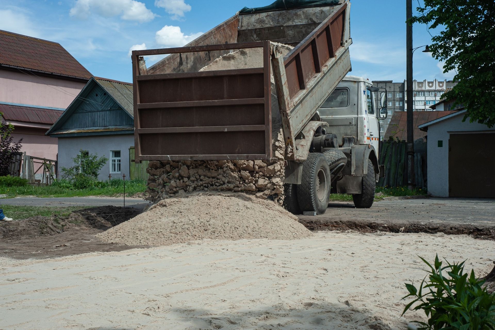 Dump truck unloading gravel onto a road in a residential area