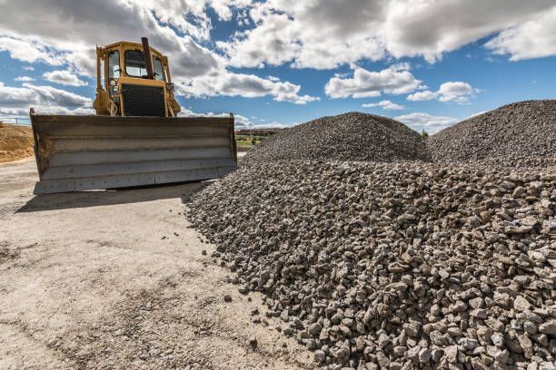 Bulldozer pushing gravel beside large rock piles under a cloudy sky