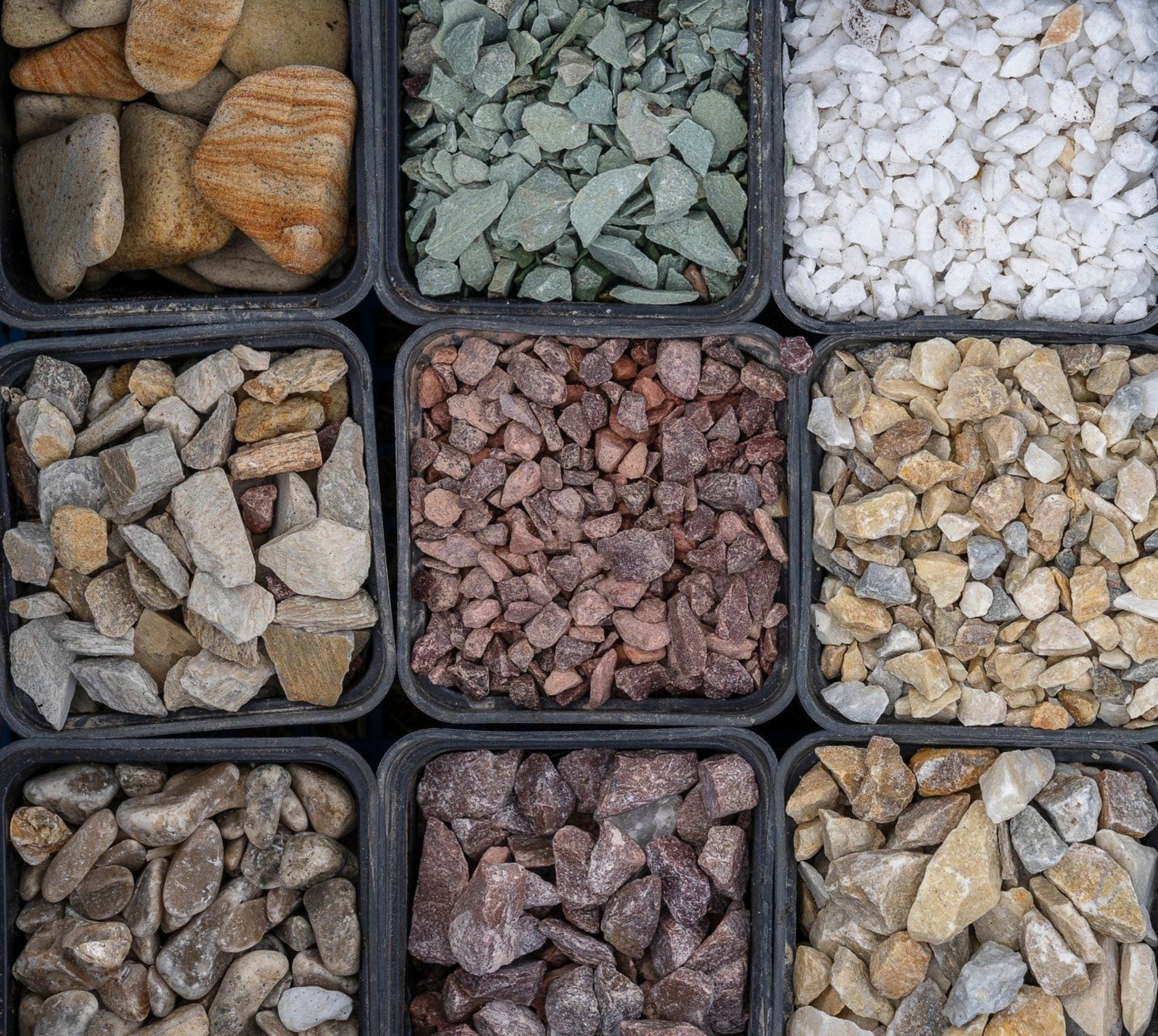 Assorted small rocks and pebbles in nine black trays, arranged in a colorful grid.