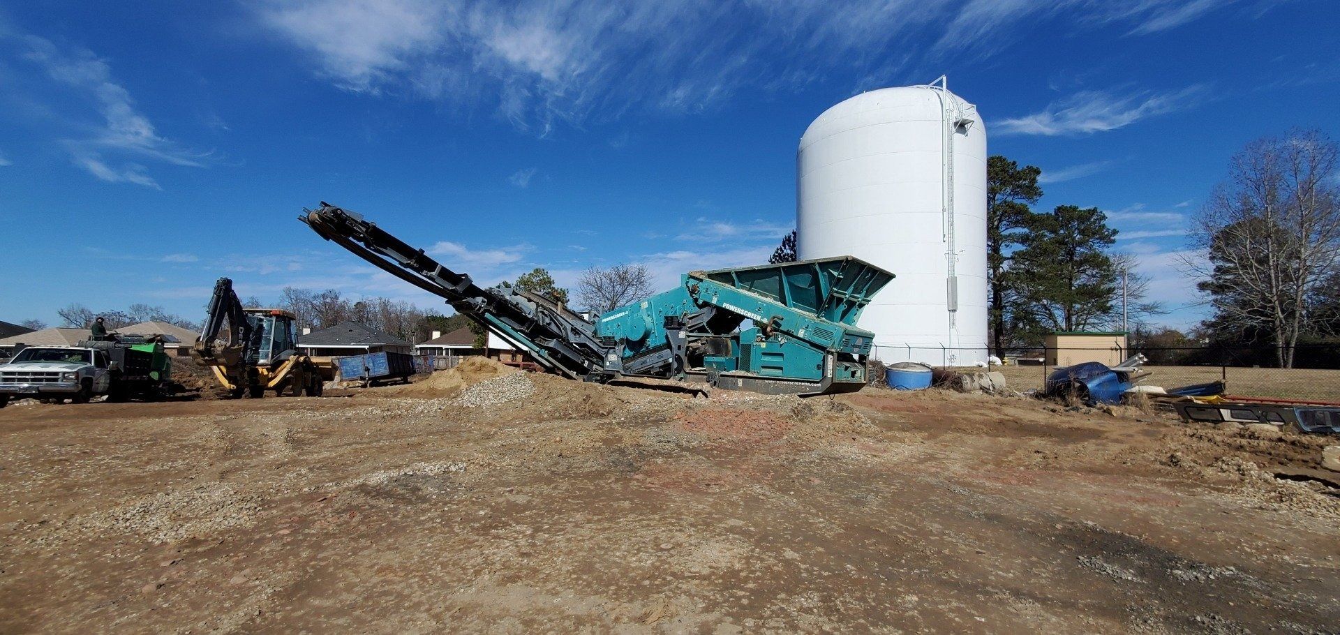 Construction site with teal machinery and a large white silo under a blue sky