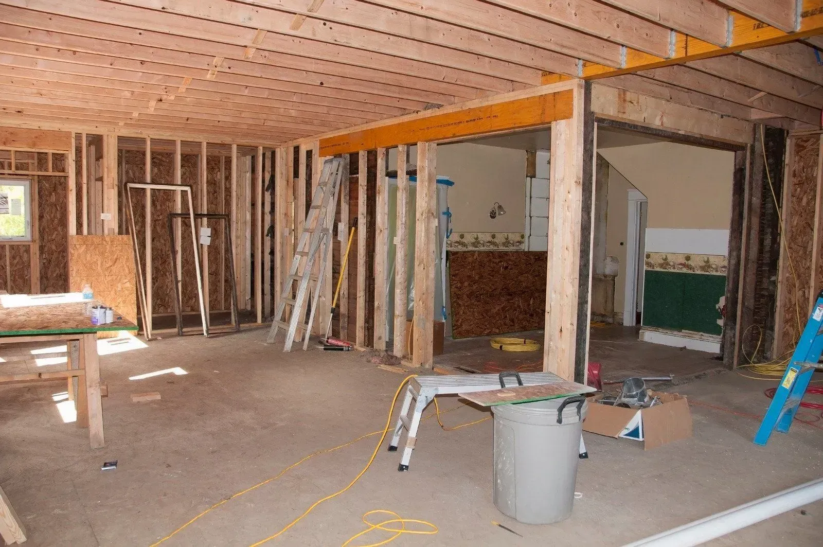 Unfinished room with exposed framing, wooden ceiling beams, tools, and construction materials on the floor
