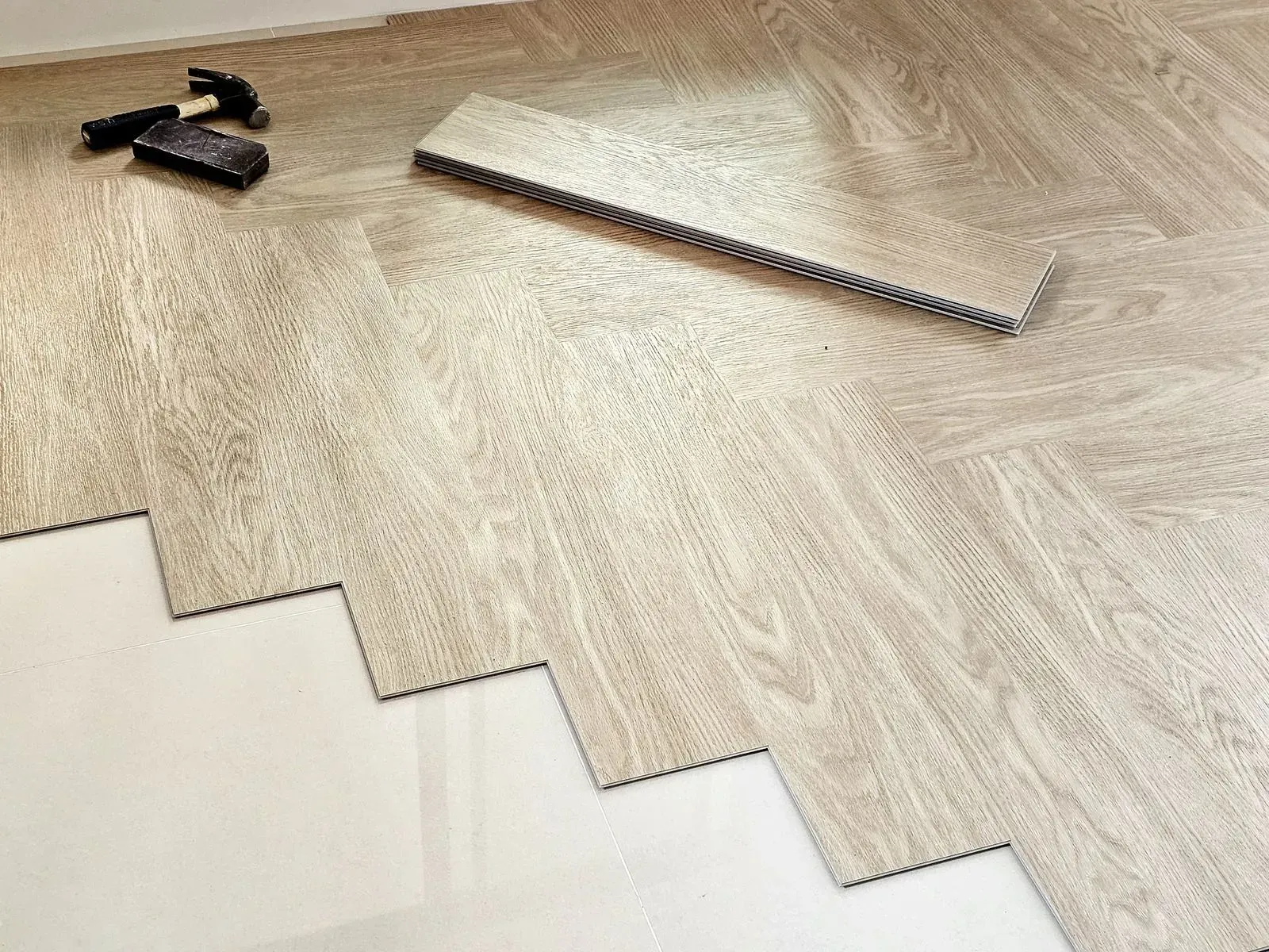 Wood-grain vinyl flooring sample with a tool and spacer on a white floor surface
