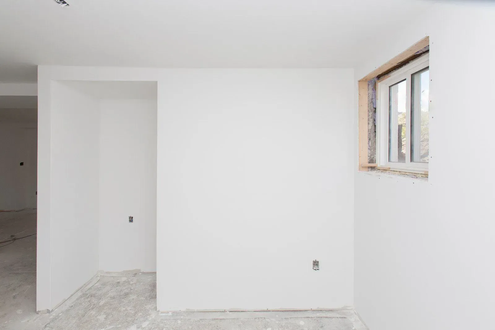 Empty white room with unfinished floor and a small window on the right wall