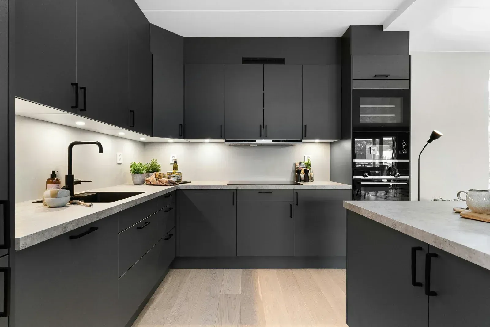 Modern dark-gray kitchen with white countertops, under-cabinet lighting, and a built-in oven.