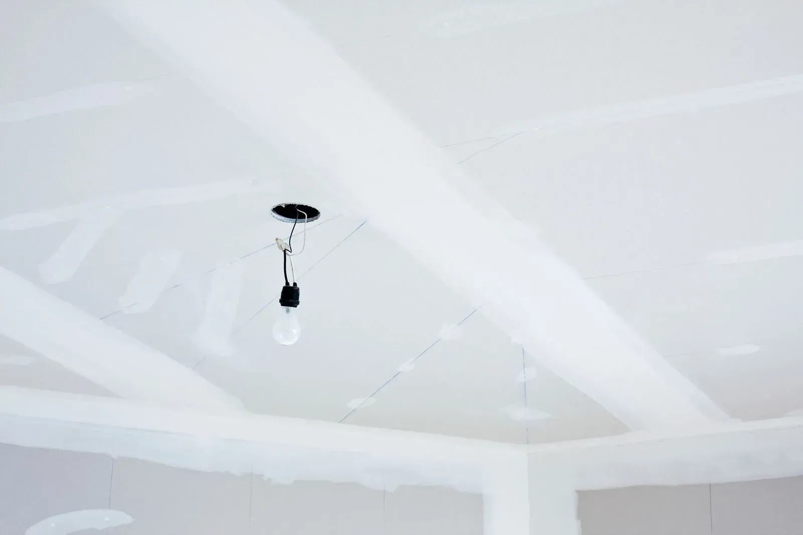 Ceiling with a hanging light bulb in a white room under construction