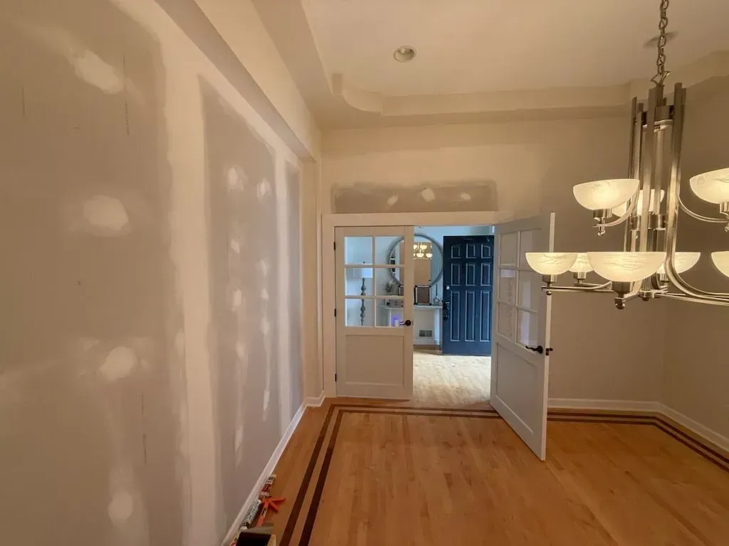 Empty dining room with hardwood floors, white walls, and a chandelier leading to a blue doorway.
