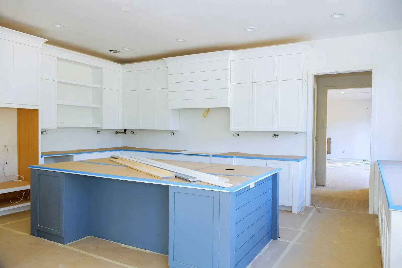 Bright kitchen under construction with white cabinets and a blue island in the center