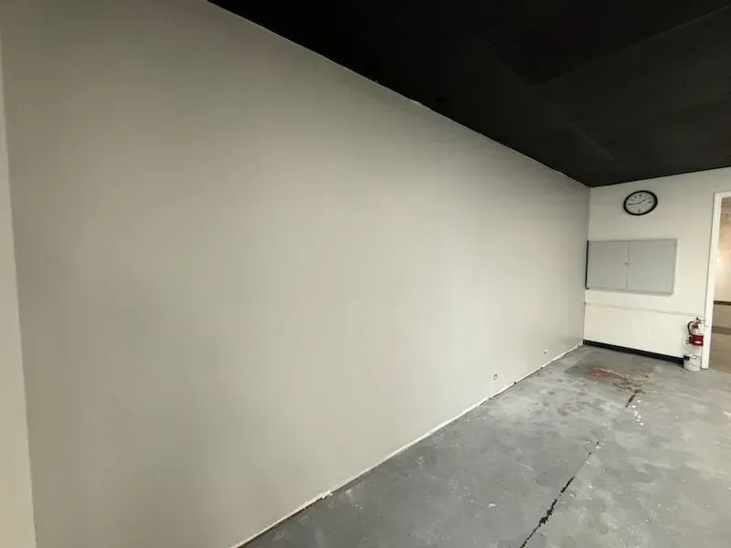 Empty room with gray walls, black ceiling, and a concrete floor, lit by daylight from a window.