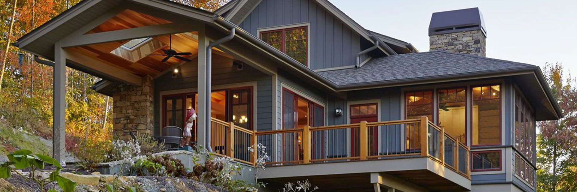 Custom home built into a wooded hillside, with a covered porch and a deck cantilevered over the slope