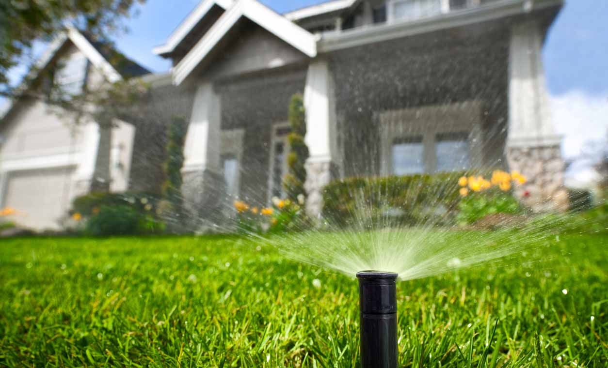 A sprinkler is spraying water on a lush green lawn in front of a house.