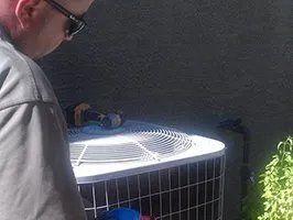 A man is working on an air conditioner outside of a building.