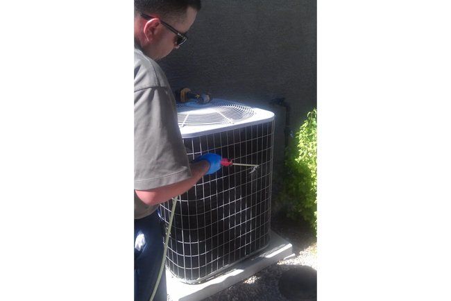 A man is cleaning an air conditioner with a hose.