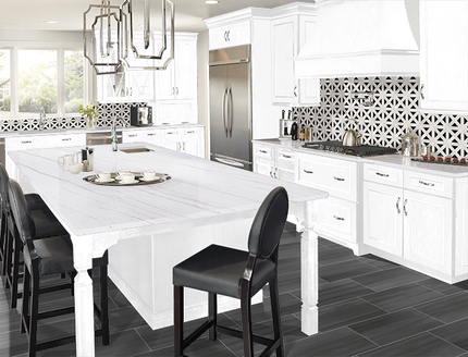 Modern white kitchen with large island, black chairs, pendant light, patterned backsplash, and stainless fridge