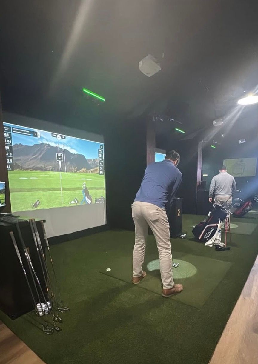 A man in a blue shirt watches a woman in a white hat on a golf green with golf balls.